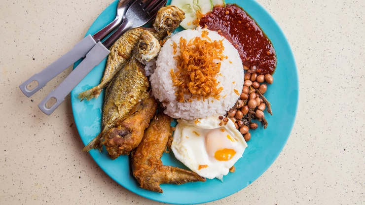 A plate of nasi lemak with fried fish, cucumber, nuts, eggs and sambal chilli