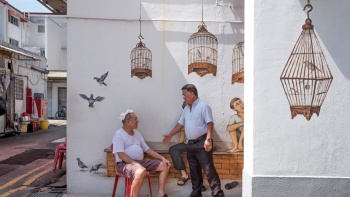 两名男子在中峇鲁成保巷 (Seng Poh Lane) 《鸟鸣角落》壁画前聊天