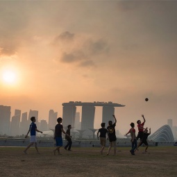 黄昏时分，一群男孩在滨海堤坝 (Marina Barrage) 上踢足球，远处是滨海湾的朦胧轮廓