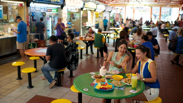 People Dining at Maxwell food centre with stalls on one side.