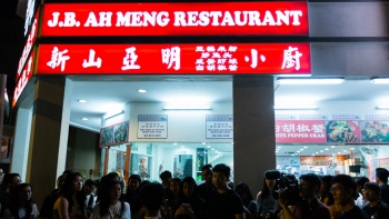 一群人站在芽笼 30 巷的<i>煮炒</i>餐馆新山亚明小厨 (JB Ah Meng) 门外等候。