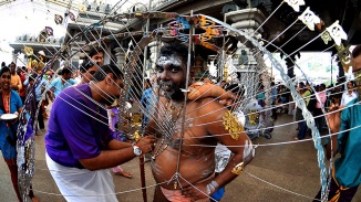 一名印度男子帮助另一名男子穿上大宝森节游行中标志性的针座铁架。