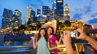 两位女士与鱼尾狮合影，背景是新加坡天际线