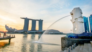 白天，鱼尾狮往新加坡河 (Singapore River) 喷出水流，背景是新加坡天际线