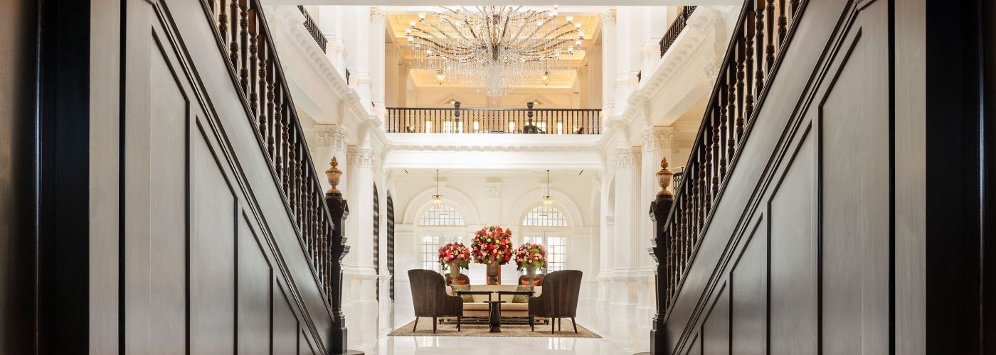 Tunnel shot of Raffles Hotel lobby, flanked by stairs on both sides with details of high ceiling and flower decoration in the center of the lobby