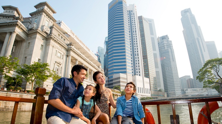 一家人在驳船上畅游新加坡河，背景是富丽敦酒店。