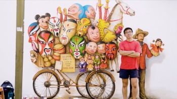 新加坡本地壁画艺术家叶耀宗站在他的穆罕默德·阿里巷壁画旁，壁画内容为街头卖面具的人